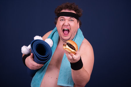 Sport, fitness and healthy lifestyle. Funny fat guy goes in for sports and eats a hamburger.の写真素材
