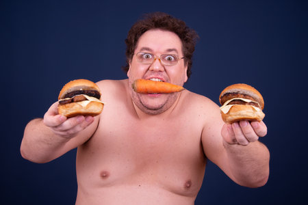 Sport, fitness and healthy lifestyle. Funny fat guy goes in for sports and eats a hamburger.の写真素材