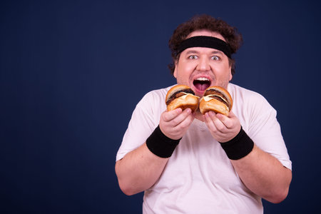 Sport, fitness and healthy lifestyle. Funny fat guy goes in for sports and eats a hamburger.