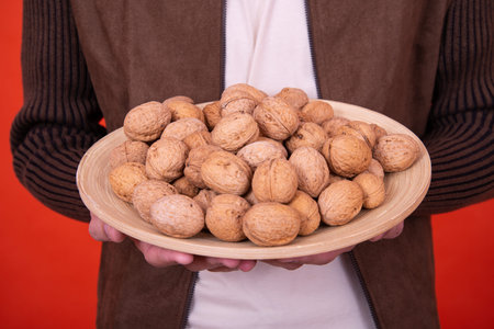 A woman holding a plate of walnuts on a red background.