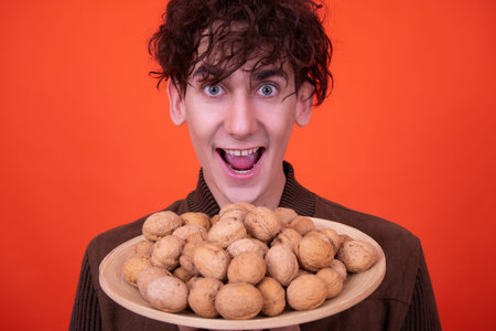 Young man holding a plate full of walnuts on a red backgroundの写真素材