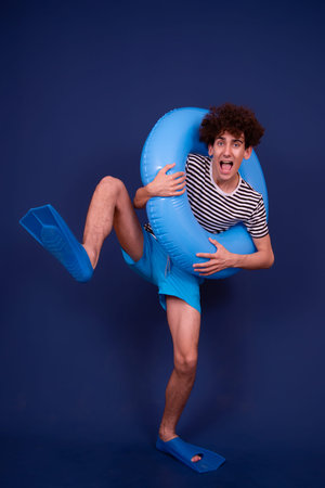 Full length portrait of a young man with afro hairstyle holding inflatable ring against blue...