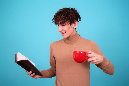 Young man with a book and a cup of coffee on a blue background