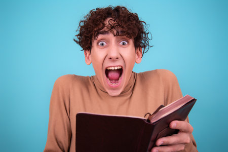 Surprised young man reading a book on a blue background.の写真素材