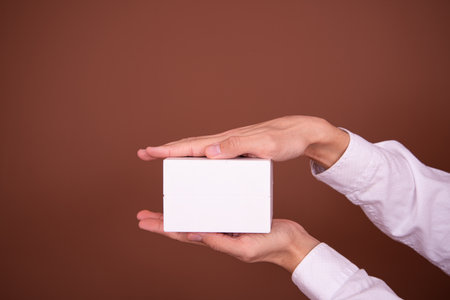Woman's hand holding a blank white business card on a brown backgroundの写真素材