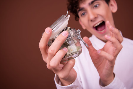 Young man holding a glass jar full of money. Money saving concept.