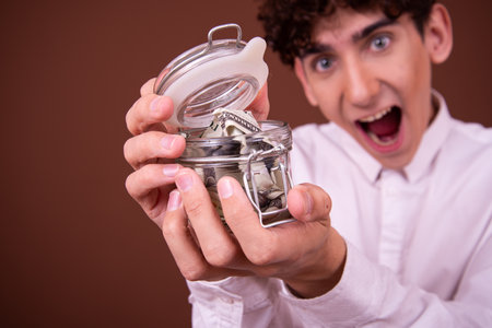 Young man holding a piggy bank full of money on brown backgroundの写真素材