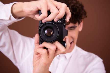 Young handsome Hispanic man with curly hair wearing white shirt against brown background