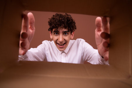 Portrait of a young man opening a cardboard box and looking insideの写真素材