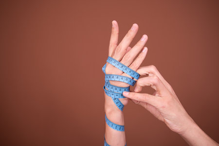 Female hands with measuring tape on brown background. Diet and weight loss conceptの写真素材