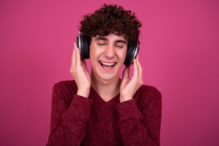 Portrait of young handsome man listening to music with headphones against pink backgroundの写真素材
