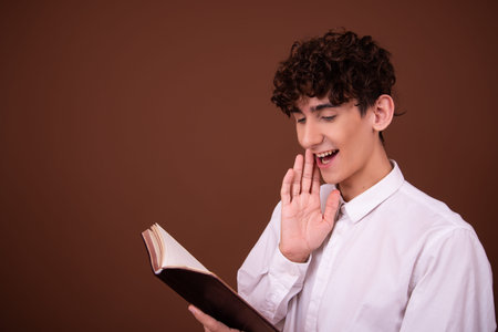 Young handsome Hispanic businessman against brown background. Man reading book and shouting
