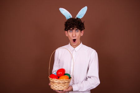 Studio shot of young handsome man against brown background wearing rabbit ears for Easterの写真素材