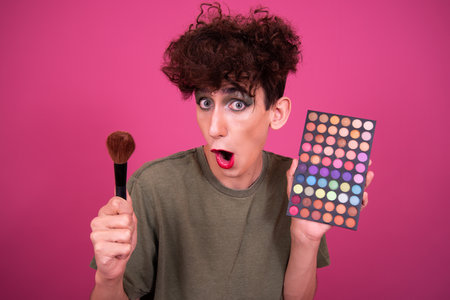 Portrait of a young man holding makeup brushes on a pink backgroundの写真素材