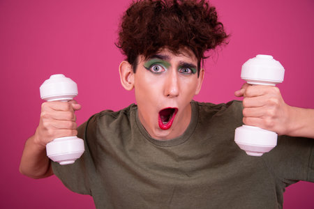 Portrait of a young man with dumbbells over pink background