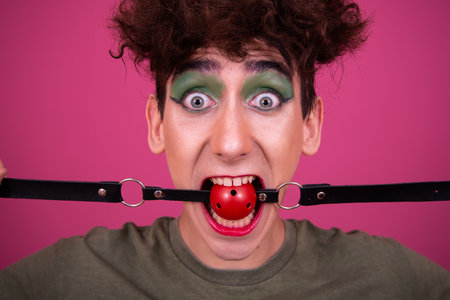 Funny young man with a red ball gag in his mouth. Studio shot.の写真素材