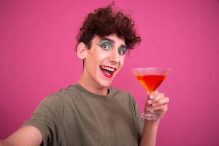 Portrait of a beautiful young woman with bright makeup holding a cocktail isolated on a pink backgroundの写真素材