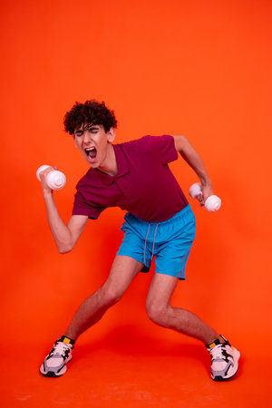 Young man in sportswear doing exercises with dumbbells on orange backgroundの写真素材