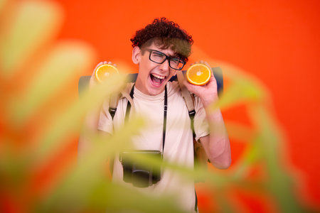 young man with a camera and an orange in his hand on a colored backgroundの写真素材