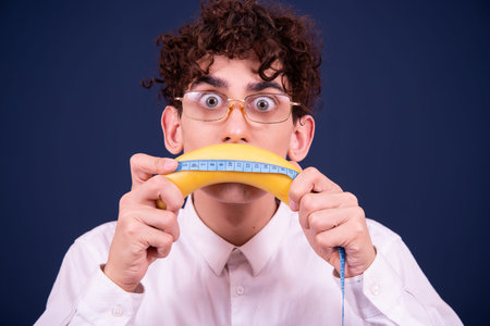 Portrait of a young man holding banana and measuring tape on blue backgroundの写真素材