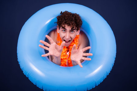 Surprised young man swimming in an inflatable ring on a blue backgroundの写真素材