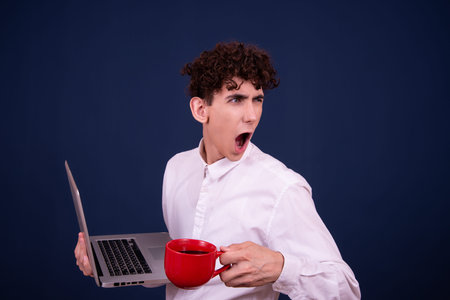 Portrait of a young man holding a laptop and a cup of coffee on a blue background