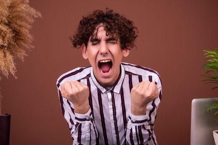 Young man with curly hair in a striped shirt is very angry.