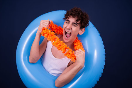 Young man with orange garland and inflatable ring on blue background