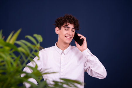 Portrait of a smiling young man talking on the phone against blue backgroundの写真素材