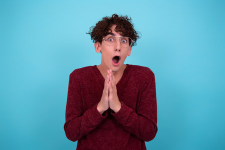 Portrait of a young man with curly hair in a red sweater on a blue background.の写真素材