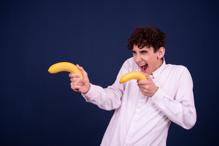 young man with a banana in his hands on a dark blue backgroundの写真素材