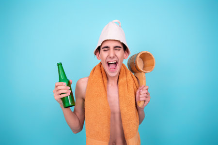 Young man in a towel with a bottle of beer and a barrel on a blue background.の写真素材