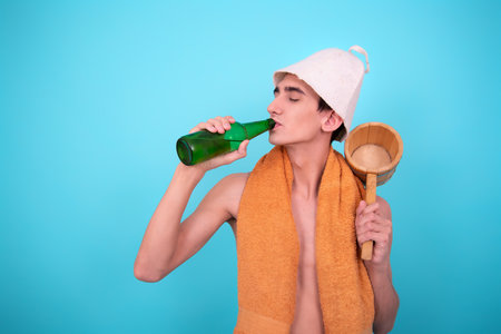 Young man in a towel with a bottle of water on a blue backgroundの写真素材
