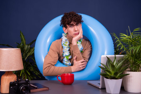 Young man with curly hair sitting at the desk in front of a blue inflatable ring.