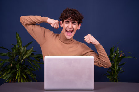 young man with a laptop on a blue background in a photo studioの写真素材