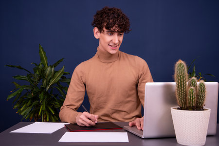 Young man sitting at the desk with a laptop and a cactusの写真素材