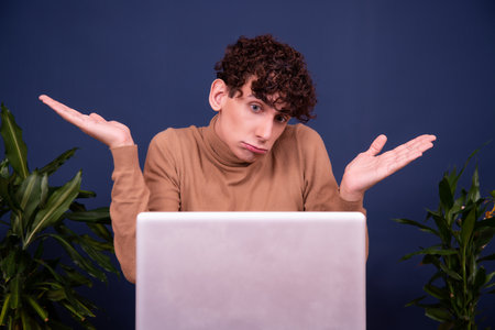 Portrait of a young man with curly hair sitting at a laptop on a blue background.の写真素材