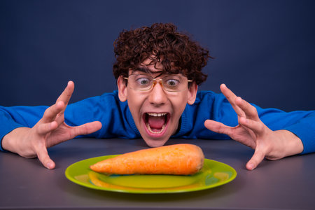 Funny boy with a carrot in a plate on a dark backgroundの写真素材