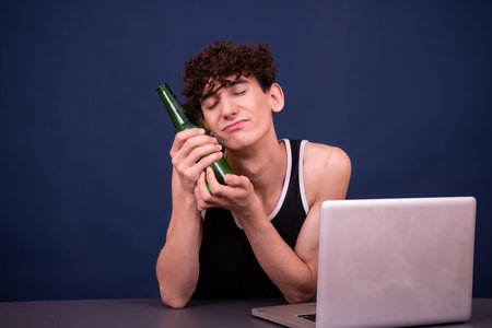 Young man drinking beer and using laptop, isolated on blue background.の写真素材