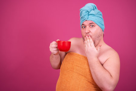 Young handsome man with towel on head holding cup of coffee isolated over pink backgroundの写真素材