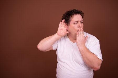 Young handsome man against brown background. Man listening with hand on earの写真素材