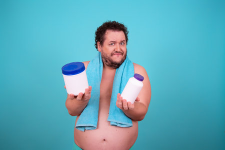 Fat man with a towel on his head holds a bottle of cream in his hands.の写真素材