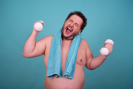 Funny fat man with dumbbells and towel on blue backgroundの写真素材
