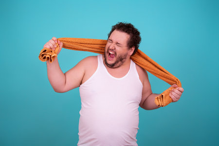 Fat man with orange towel on his head. Isolated on blue background.の写真素材