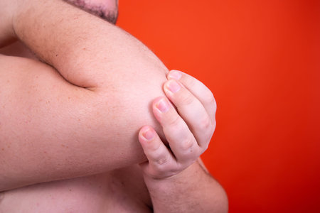 Man suffering from elbow pain on a red background. Close-up.