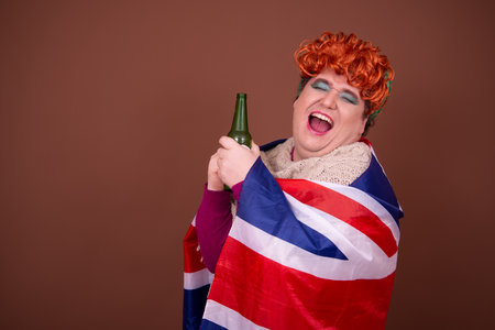 Young beautiful woman with red hair against brown background holding a beer bottleの写真素材