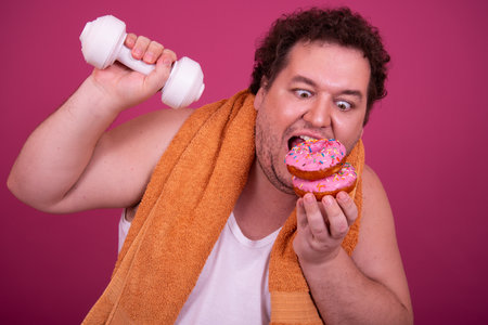 Fat man with dumbbells and donut isolated on pink backgroundの写真素材