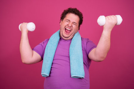 Fat man with dumbbells and towel isolated on pink background.の写真素材