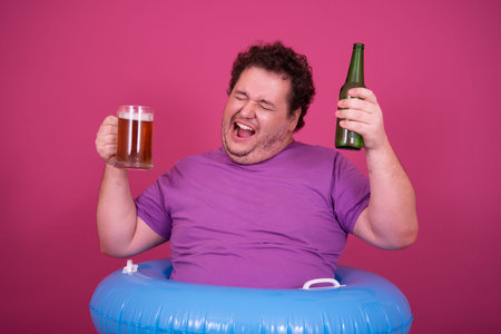 Funny fat man with beer and inflatable ring on pink background