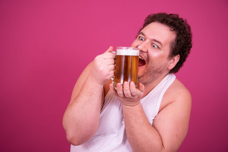 Portrait of a funny fat man drinking beer isolated over pink background